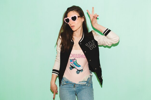 Young hipster beautiful woman, funny heart sunglasses, against blue wall, cool face expression