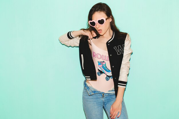 young hipster beautiful woman, funny heart sunglasses, against blue wall, non-isolated, cool face expression