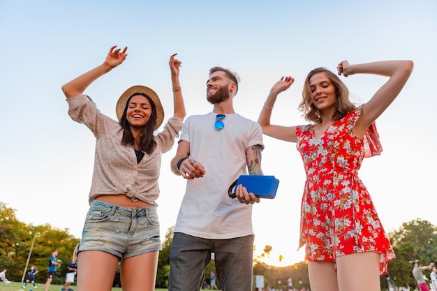 Foto gratuita giovane compagnia hipster di amici che si divertono insieme nel parco sorridendo ascoltando musica su altoparlanti wireless