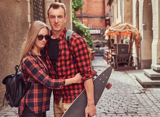 Young hipster couple, handsome skater and his girlfriend cuddling while standing on an old Europe street.