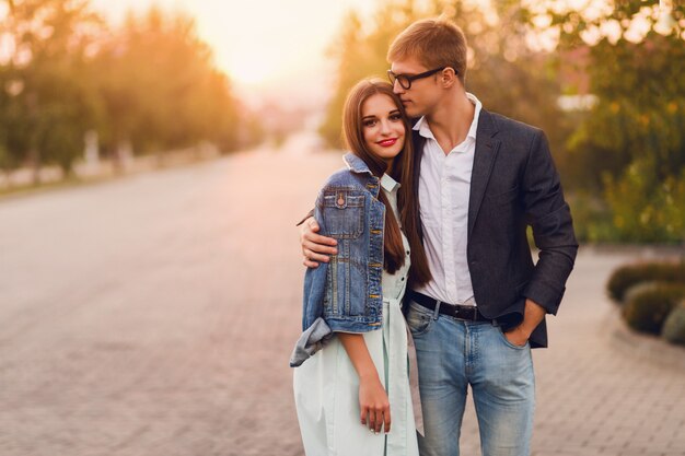 Young hipster couple in love outdoor. Stunning sensual portrait of young stylish fashion couple posing in summer sunset . Pretty young girl in jeans jacket and her handsome boyfriend walking .