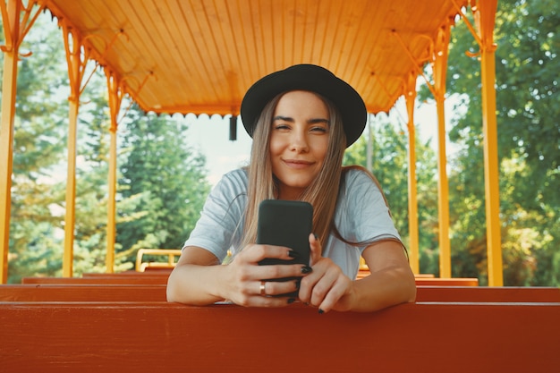 Young hipster girl in trendy hat holding smartphone in hands