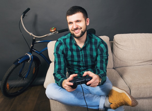 Young hipster handsome bearded man sitting on couch at home, playing video game on notebook