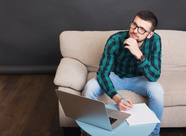 Uomo barbuto bello giovane hipster che si siede sul divano a casa