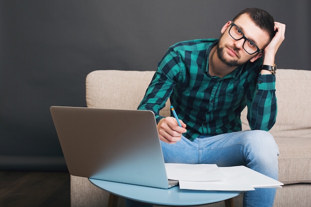 Young hipster handsome bearded man sitting on couch at home