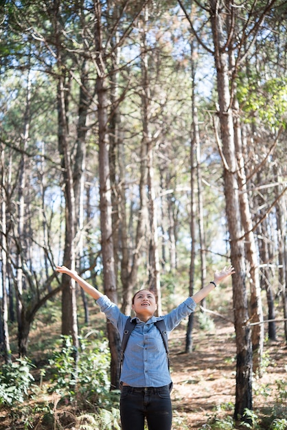 Young hipster happy woman enjoy nature in forest with outstretched arms.