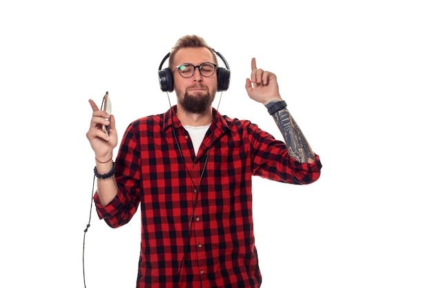 Young hipster man in checkered shirt and glasses wearing earphones looking happy on white background. Studio shot. Copy space