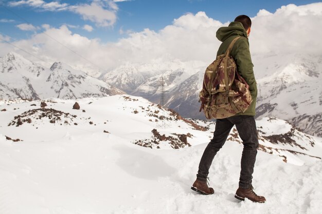 Young hipster man hiking in mountains, winter vacation traveling