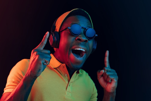 young hipster man listening music with headphones at black studio with neon lights.