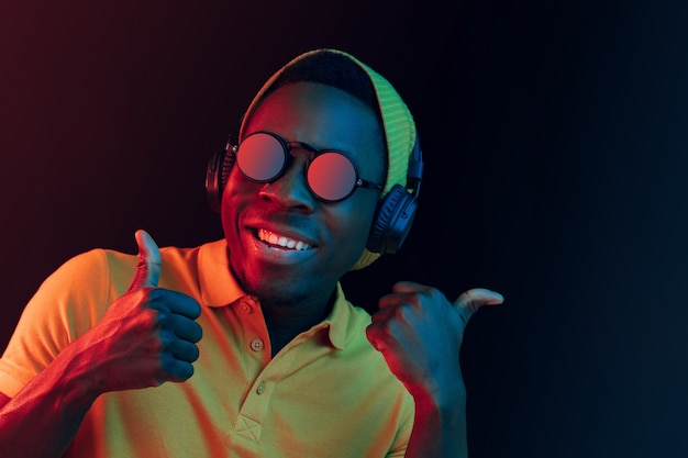 young hipster man listening music with headphones at black studio with neon lights.