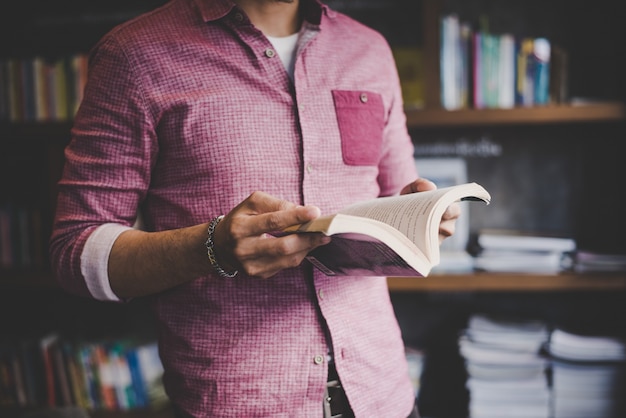 Free photo young hipster man reading book in library.