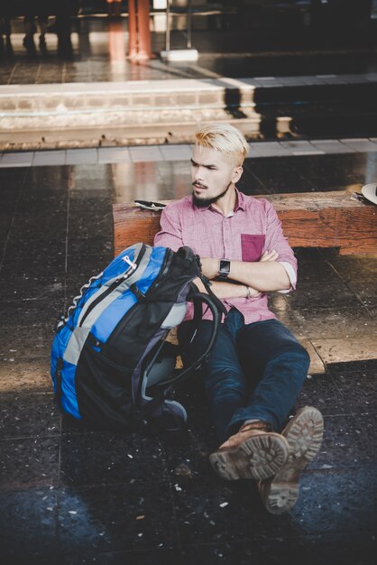 Young hipster man sitting on wooden bench at train station. Man sitting waiting for the train at platform.