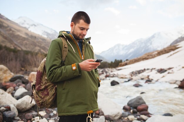 Young hipster man using smartphone, wild nature, winter vacation, hiking