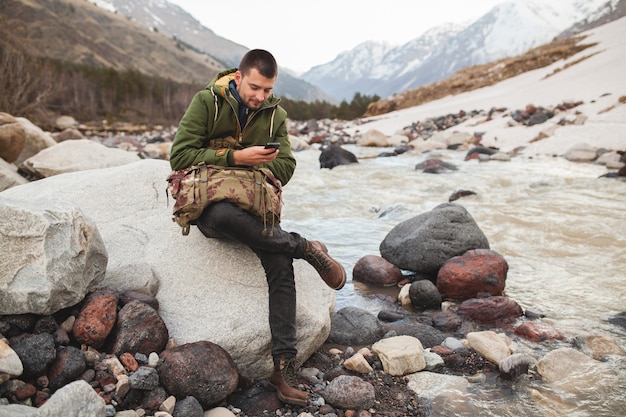 Young hipster man using smartphone, wild nature, winter vacation, hiking