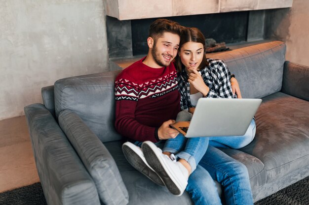 Young hipster smiling man and woman sitting at home in winter, looking laptop with surprised exited interested face expression, couple on leisure together, studying online, freelancer, happy, dating