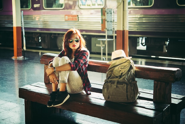 Молодая женщина-хипстер турист с рюкзаком, сидя на вокзале. Праздничная туристическая концепция.