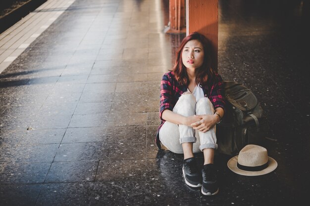 Young hipster tourist woman with backpack sitting in the train station. Holiday tourist concept.