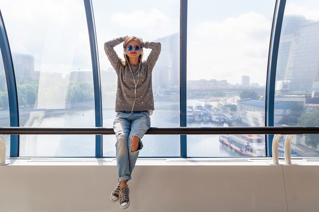 Young hipster woman in casual outfit having fun listening to music in headphones