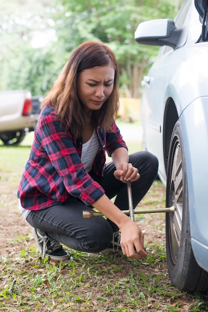 彼女の車のフラットタイヤをチェックアウト若いhipster女性は修正しようとします。