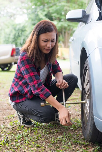 Молодая женщина-хипстер, проверяя плоскую шину на своей машине, пытается ее исправить.