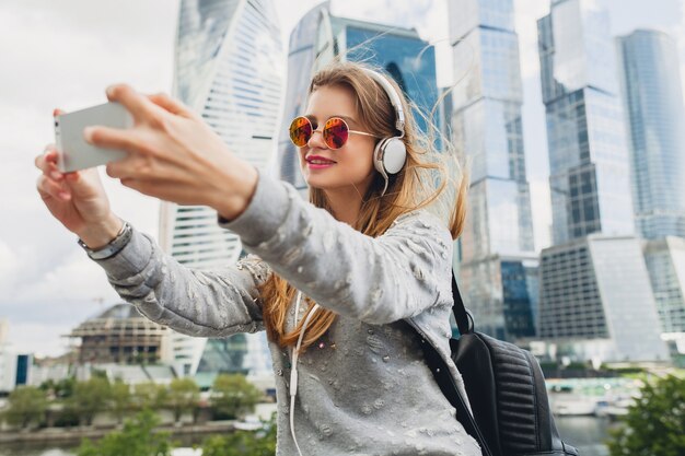 Young hipster woman having fun in street listening to music on headphones