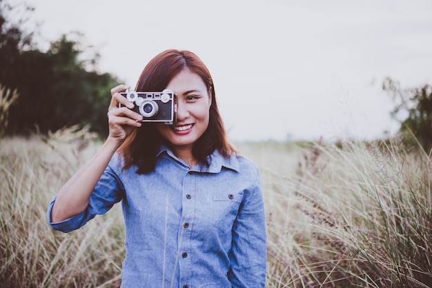 Young hipster woman making photos with vintage film camera at summer field. Women lifestyle concept.