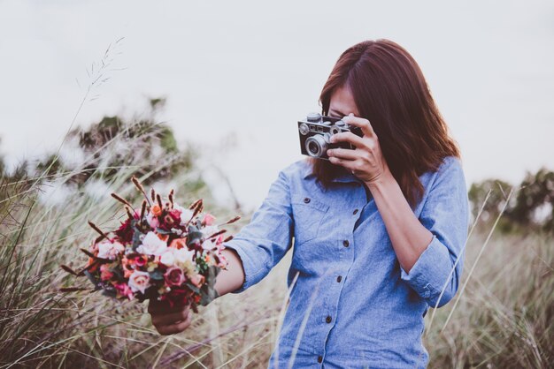 夏のフィールドでヴィンテージフィルムカメラで写真を作る若いヒップスターの女性。女性のライフスタイルのコンセプト。