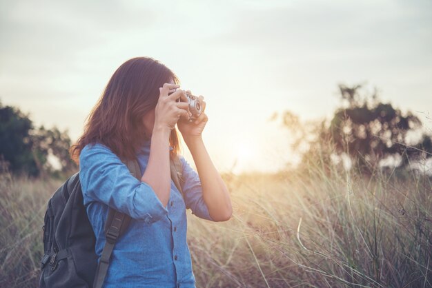 Young hipster woman making photos with vintage film camera at summer field. Women lifestyle concept.