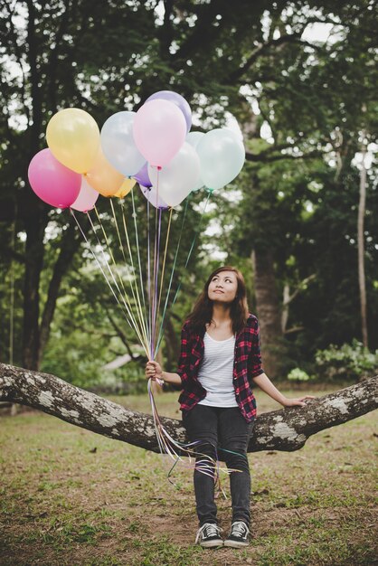 Молодая женщина хипстер, сидя на ветке дерева с красочные воздушные шары в руке, расслабляющий пользуются праздник.