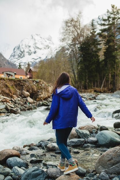 Молодая хипстерская женщина, идущая на скалах у реки в зимнем лесу