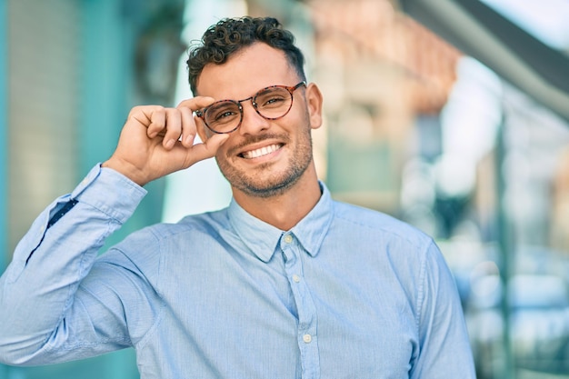 Young hispanic businessman smiling happy touching his glasses at the city.