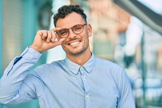 ヒスパニック系の若い実業家が街で眼鏡に触れて幸せな笑顔を浮かべています。