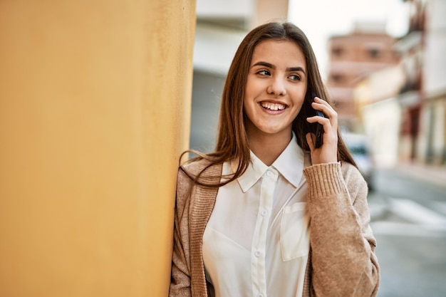 Молодая латиноамериканская деловая женщина улыбается, счастливо разговаривая по смартфону в городе.