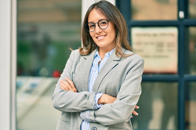 Young hispanic businesswoman with arms crossed smiling happy at the city.