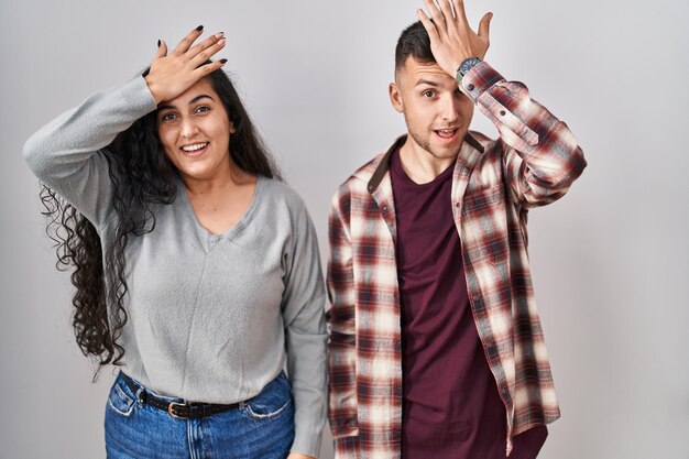 Young hispanic couple standing over white background surprised with hand on head for mistake, remember error. forgot, bad memory concept.