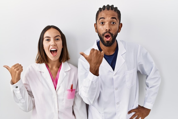 Free photo young hispanic doctors standing over white background surprised pointing with hand finger to the side open mouth amazed expression