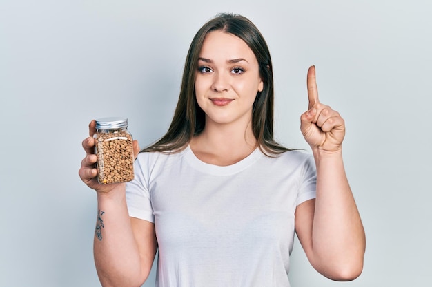 Free photo young hispanic girl holding lentils bowl smiling with an idea or question pointing finger with happy face number one