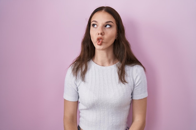 Foto gratuita giovane ragazza ispanica in piedi su sfondo rosa che fa la faccia di pesce con le labbra, gesto pazzo e comico. espressione buffa.