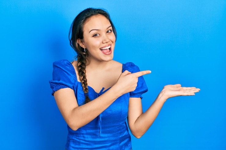 Free Photo young hispanic girl wearing casual clothes amazed and smiling to the camera while presenting with hand and pointing with finger