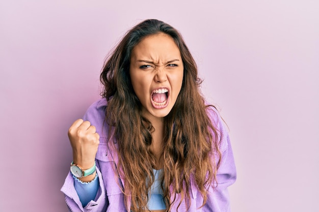 カジュアルな服を着たヒスパニック系の若い女の子は、怒りと攻撃的なコンセプトで叫びながら、欲求不満と激怒の拳を上げて怒って怒っています