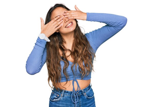 Young hispanic girl wearing casual clothes covering eyes with hands smiling cheerful and funny. blind concept.