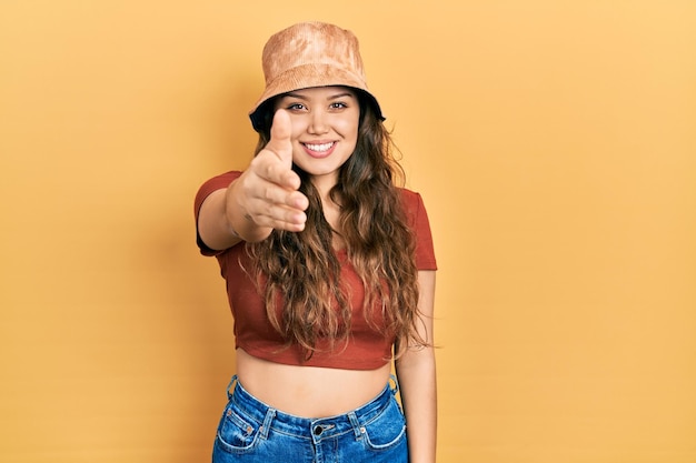 Free photo young hispanic girl wearing casual clothes and hat smiling friendly offering handshake as greeting and welcoming successful business