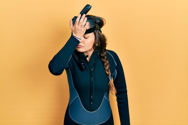 Free photo young hispanic girl wearing diver neoprene uniform surprised with hand on head for mistake remember error forgot bad memory concept