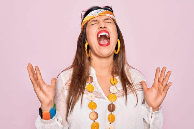 Free photo young hispanic hippie woman wearing fashion boho style and sunglasses over pink background celebrating mad and crazy for success with arms raised and closed eyes screaming excited winner concept