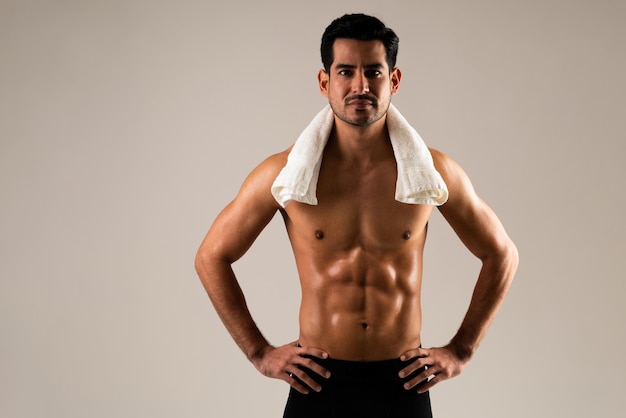 Молодой латиноамериканский спортсмен с полотенцем на шее и руками на бедрах