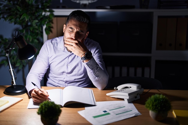 Free photo young hispanic man business worker writing on notebook working overtime at office