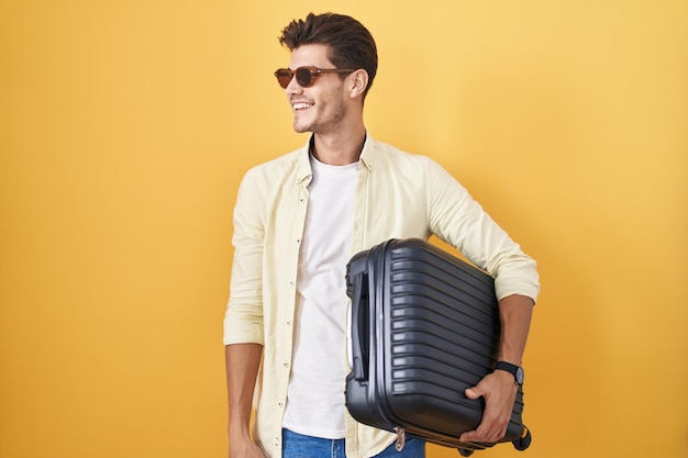 Бесплатное фото Молодой латиноамериканец с чемоданом, собираясь на летние каникулы, смотрит в сторону с улыбкой на лице, естественным выражением лица и уверенным смехом
