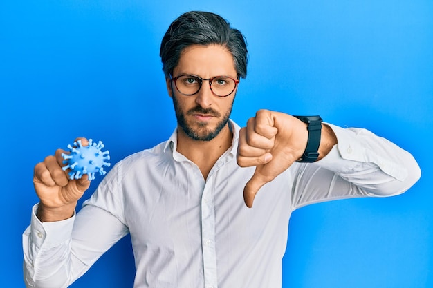 Free photo young hispanic man holding virus toy with angry face negative sign showing dislike with thumbs down rejection concept