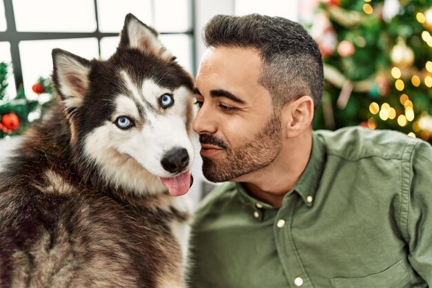 自宅のクリスマス ツリーのそばのソファーに座っていた犬にキスをするヒスパニック青年