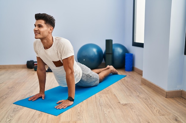 Young hispanic man smiling confident stretching at sport center